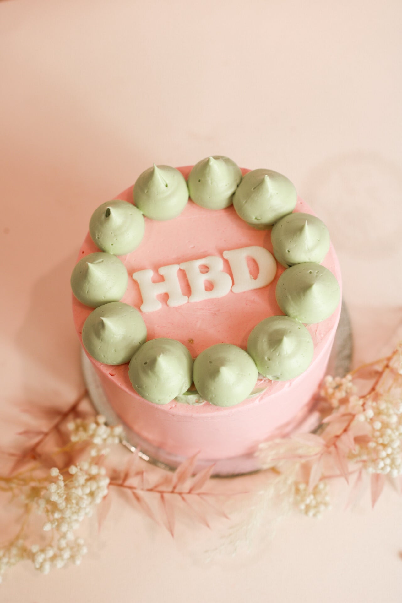 Pink bento cake with green decor and three letters HBD on top