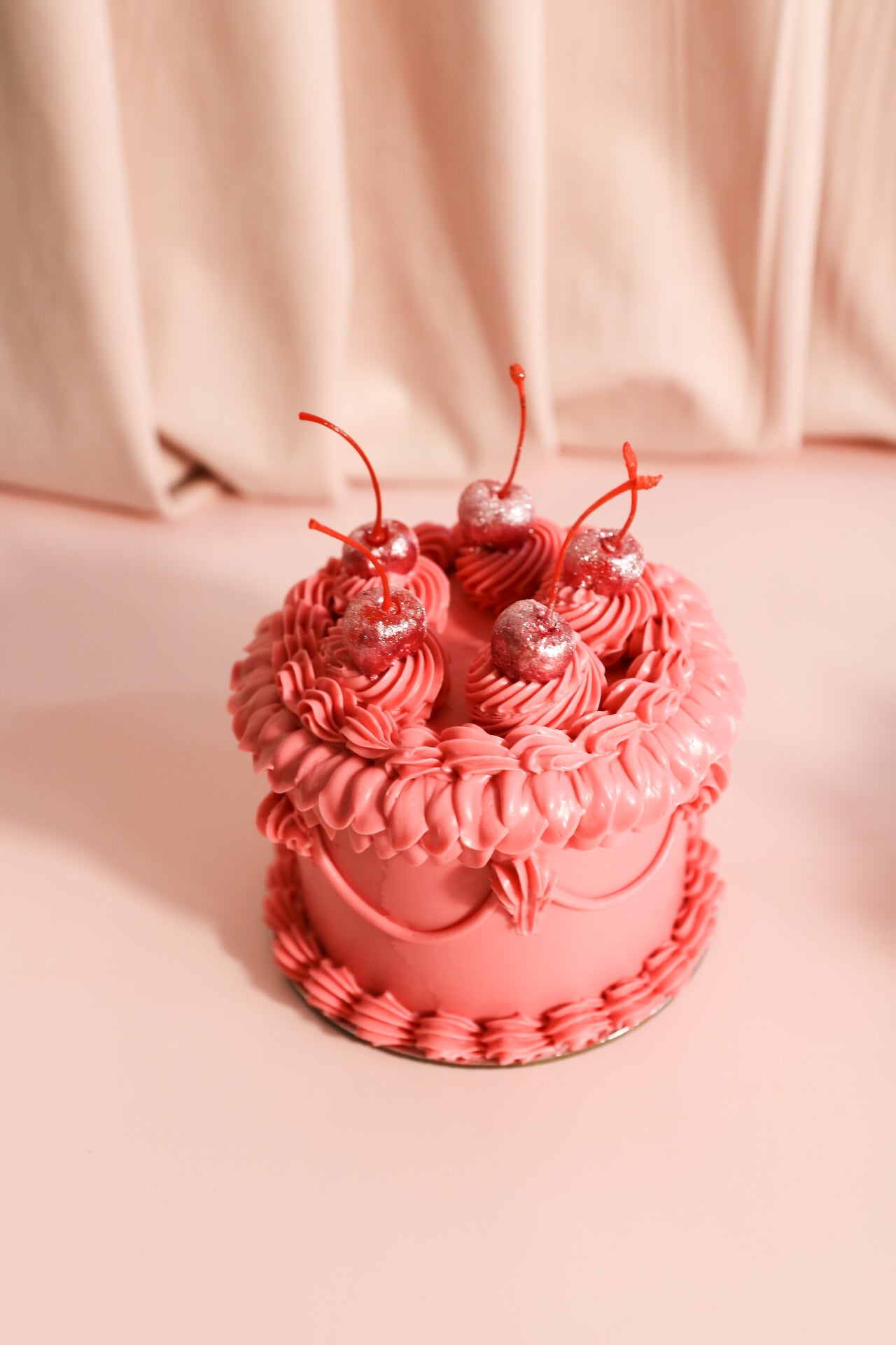 Pink cake with pink cream ruffles and five glittery red cherries on top of the cake.