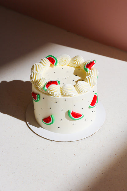 White cake with white cream ruffles and watermelon slices around the cake.