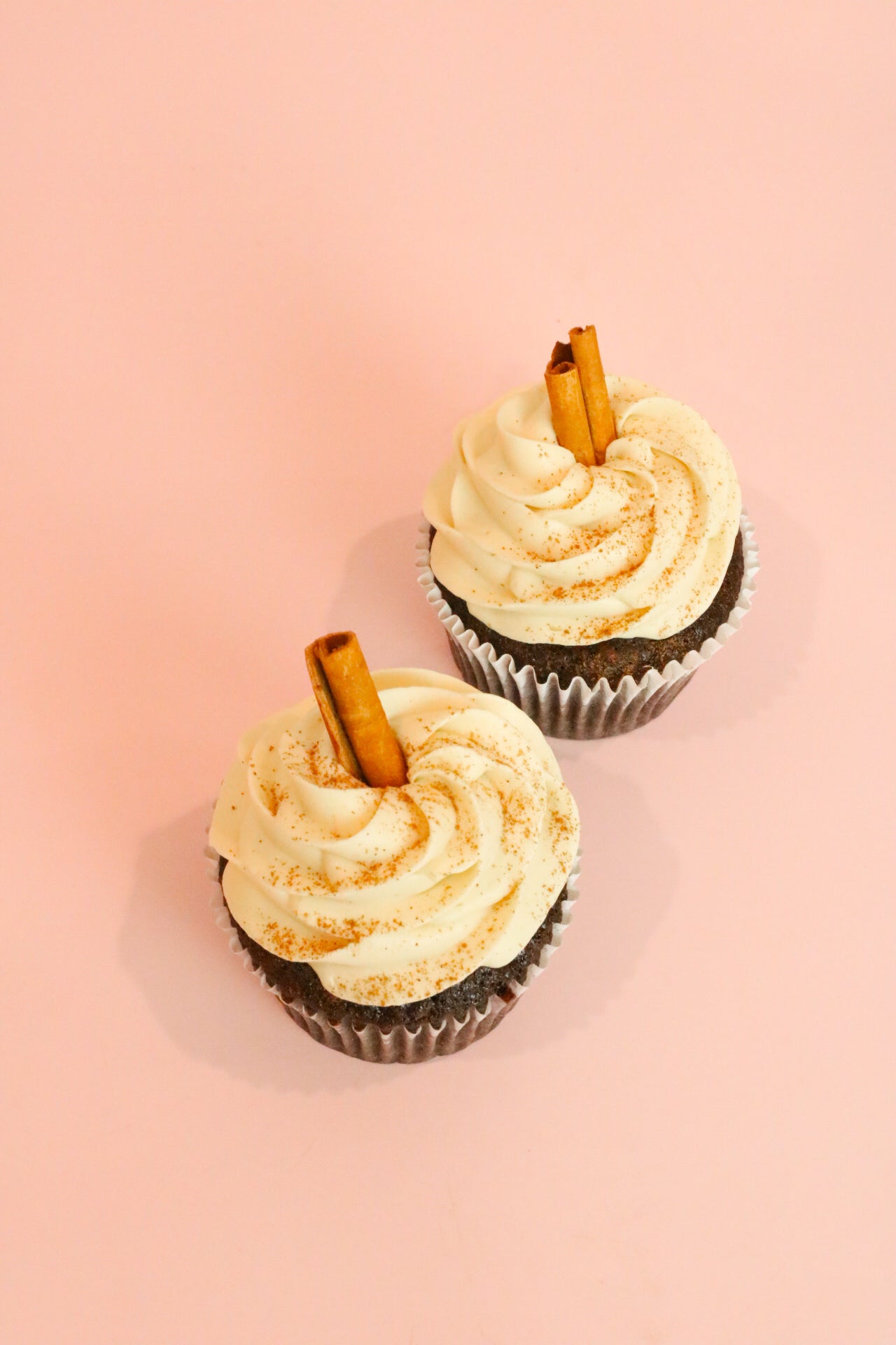 Two cupcakes with white cream decor sprinkled with cinnamon and cinnamon stick on top of it