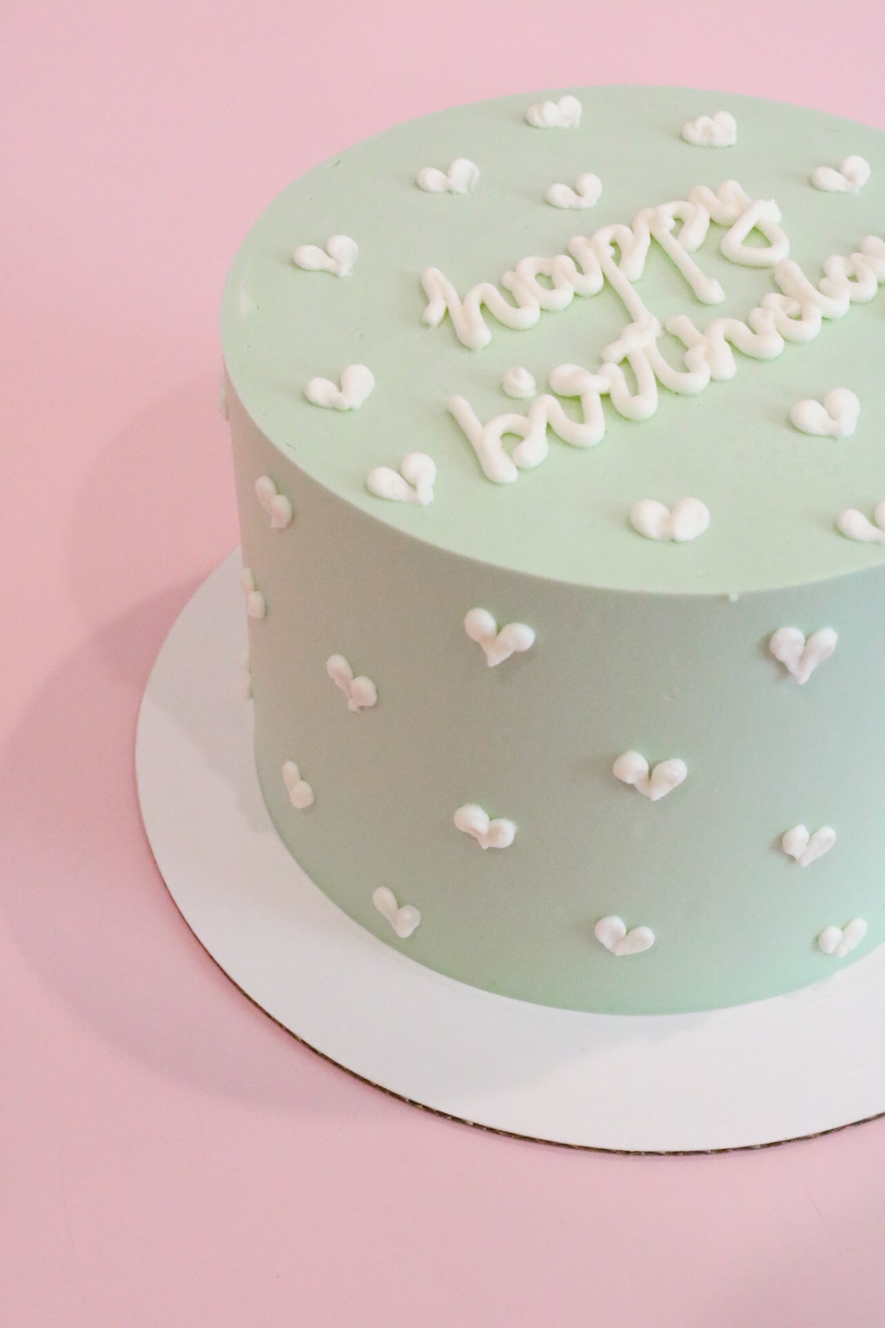 Light green cake with small white hearts and caption happy birthday.