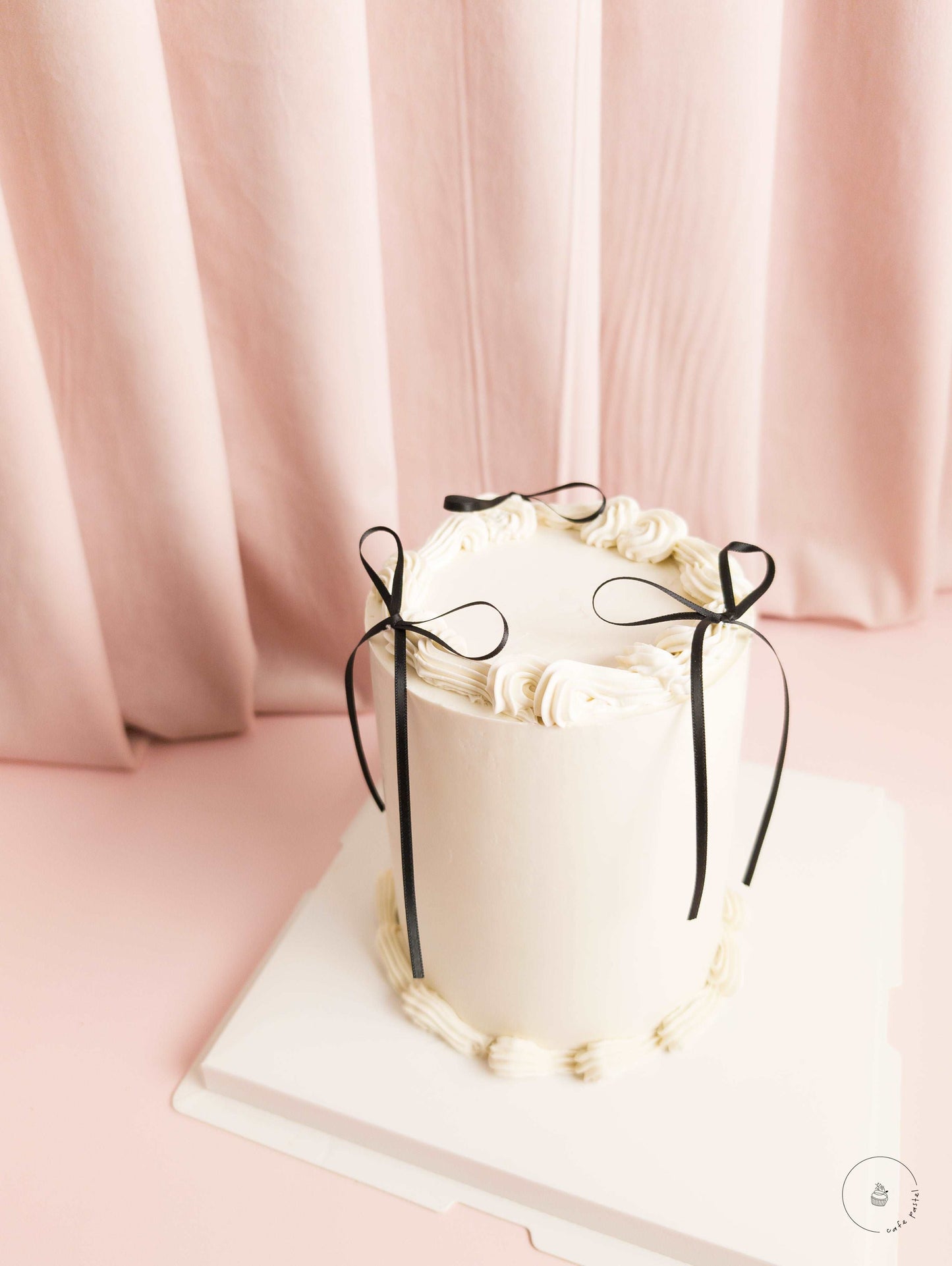 High ivory cake with three black ribbons and cream ruffles on top of it.