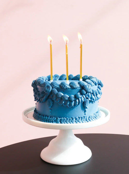 Blue cake with blue cream ruffles on top of the cake and three birthday candles.